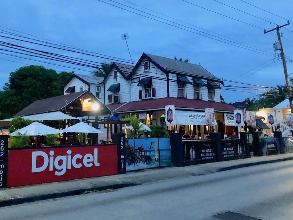 Exterior view of Mojo Bar, one of the best restaurants in Bridgetown. Mojo is a white building with a red awning and white umbrellas outside.