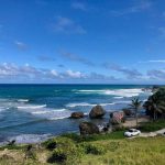 A coastal view of Bathsheba, one of the best Caribbean surfing destinations. There's a pink structure on a rock and a few cars parked along the road