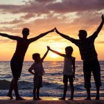 A family standing on the beach at sunset holding hands