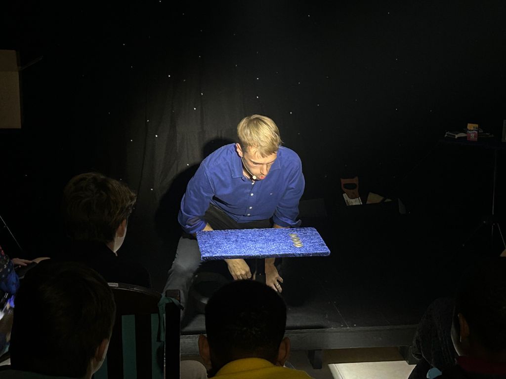 Hans leaning over a blue table with coins on it, preparing for a close-up magic trick
