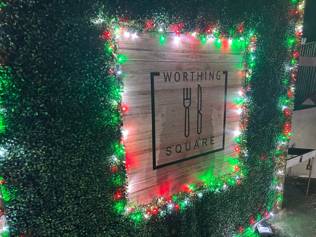 The welcome sign for Worthing Square surrounded in red and green Christmas lights